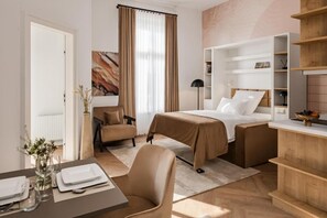 Una habitación de hotel con una cama, una silla, un escritorio con un florero y una estantería.