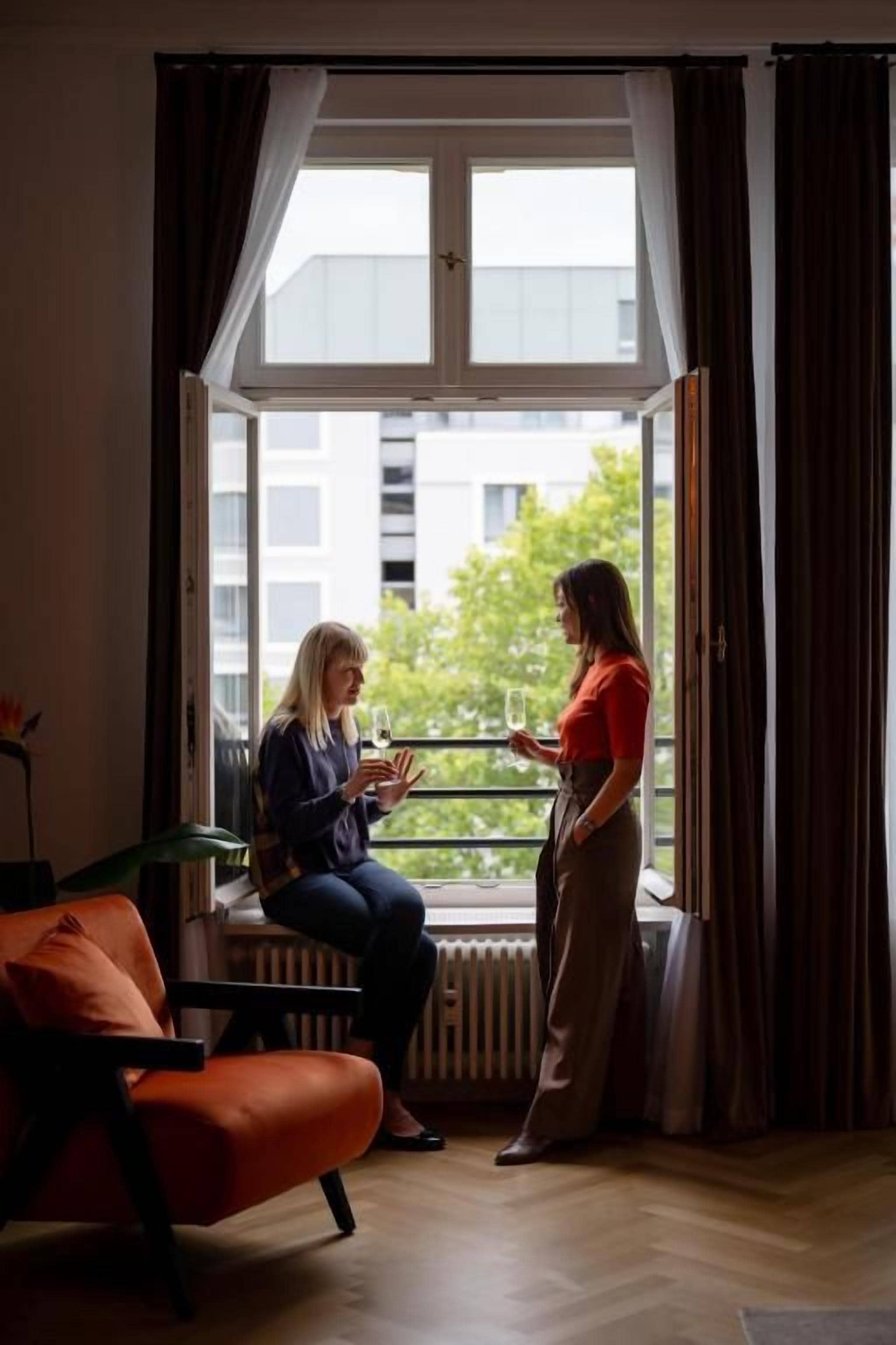 A room with a large window, a radiator, an orange chair, and a table.