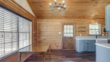 A wooden interior with a dining table, a chandelier, and a kitchen area.