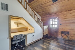 Um quarto com escada de madeira, uma mesa com cadeira e uma porta com janela.
