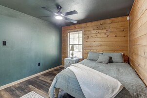 Un dormitorio con cama, mesita de noche, ventana con persianas y ventilador de techo.