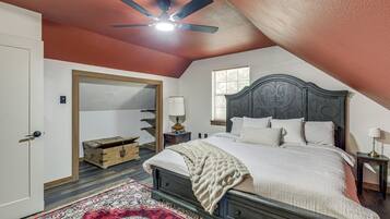 A bedroom with a sloped ceiling, a bed with a dark headboard, a wooden chest, a red and white patterned rug, and a window with blinds.