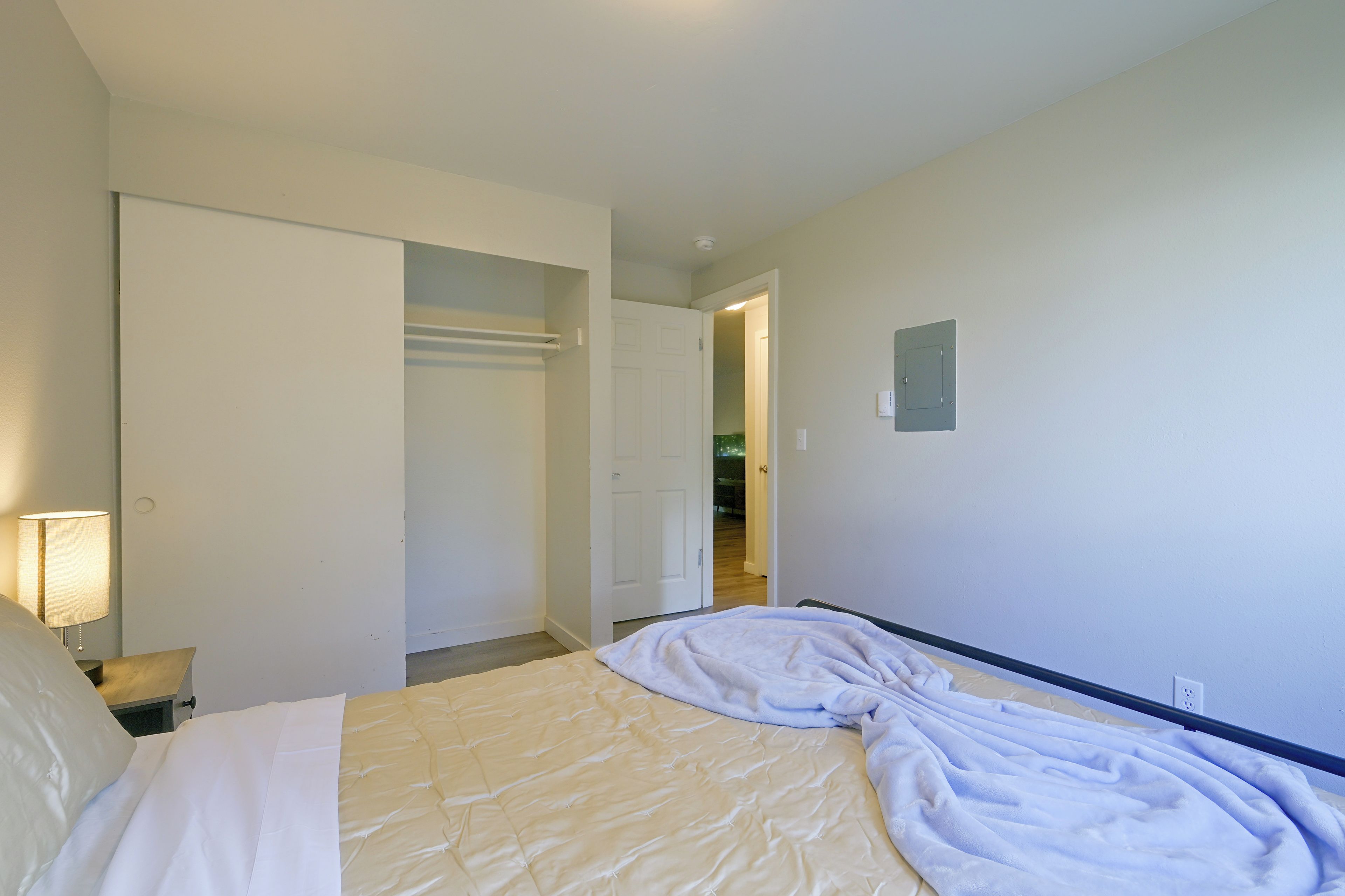 Een hotelkamer met een bed, een nachtkastje, een lamp, een kast en een deur die naar een andere kamer leidt.