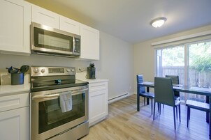Una cocina con armarios blancos, un microondas, una estufa y un comedor con mesa y sillas.