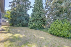 A backyard with a grassy lawn, a wooden deck, and dense foliage including tall trees and shrubs. - 3 Mi to Olympia! Apt w/ Shared Laundry (Lacey)