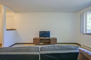 Una sala de estar con un televisor de pantalla plana sobre un soporte de madera, una puerta y una ventana.
