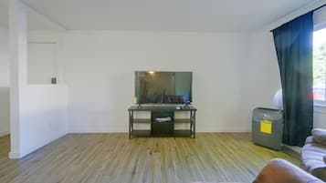 A room with a wooden floor, a desk with a mirror, a television, a small heater, and a sofa.