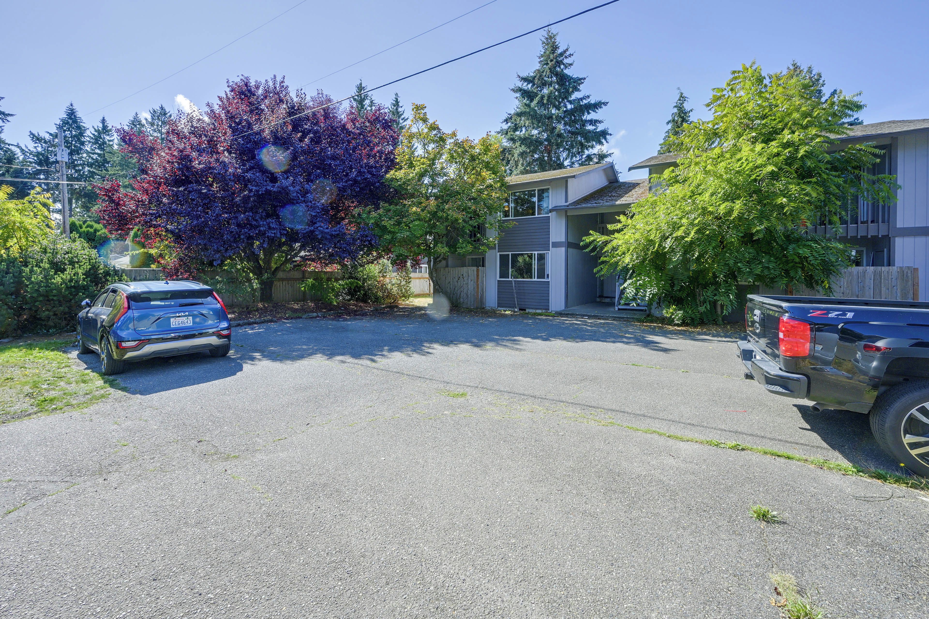 A residential driveway with two cars parked, surrounded by trees and a house.