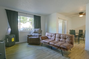 A room with a brown leather sofa, a grey armchair, a dining table with chairs, a ceiling fan, and a window with curtains. - Centrally Located Lacey Escape: 2 Mi to Hospital (Lacey)