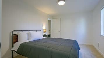 A bedroom with a single bed, a nightstand, a lamp, and a door leading to another room.