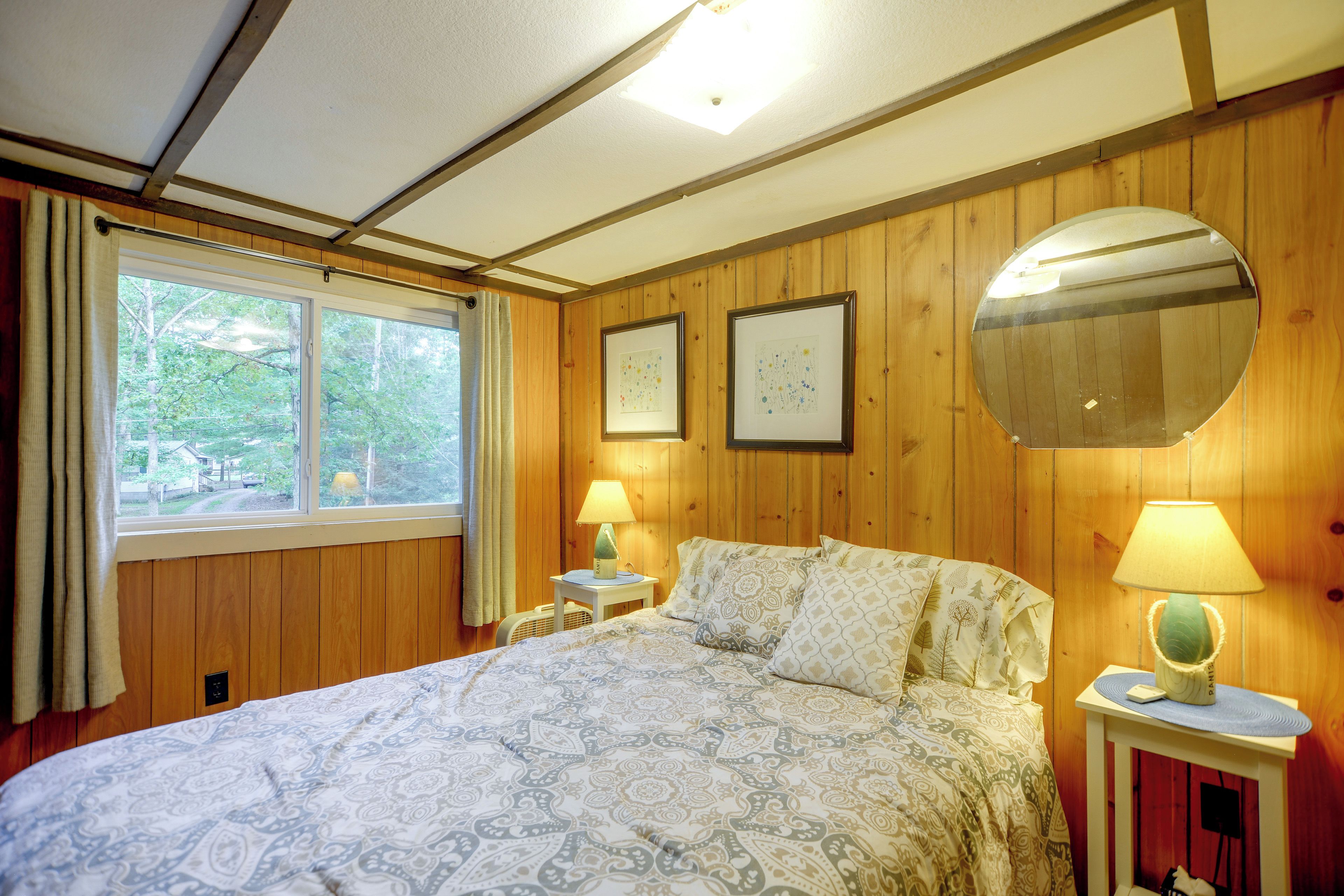 A bedroom with a bed, two bedside lamps, a round mirror, and two framed artworks on the wall.