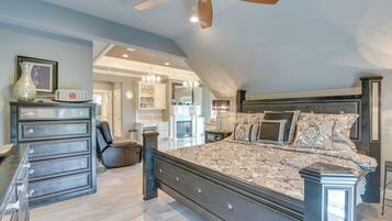 A spacious bedroom with a large bed, a dresser, a ceiling fan, and a view of the adjacent bathroom.