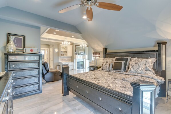 A spacious bedroom with a large bed, a dresser, a ceiling fan, and a view of the adjacent bathroom.