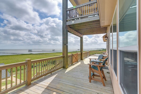 A wooden deck with outdoor seating, overlooking a grassy area and a pier.