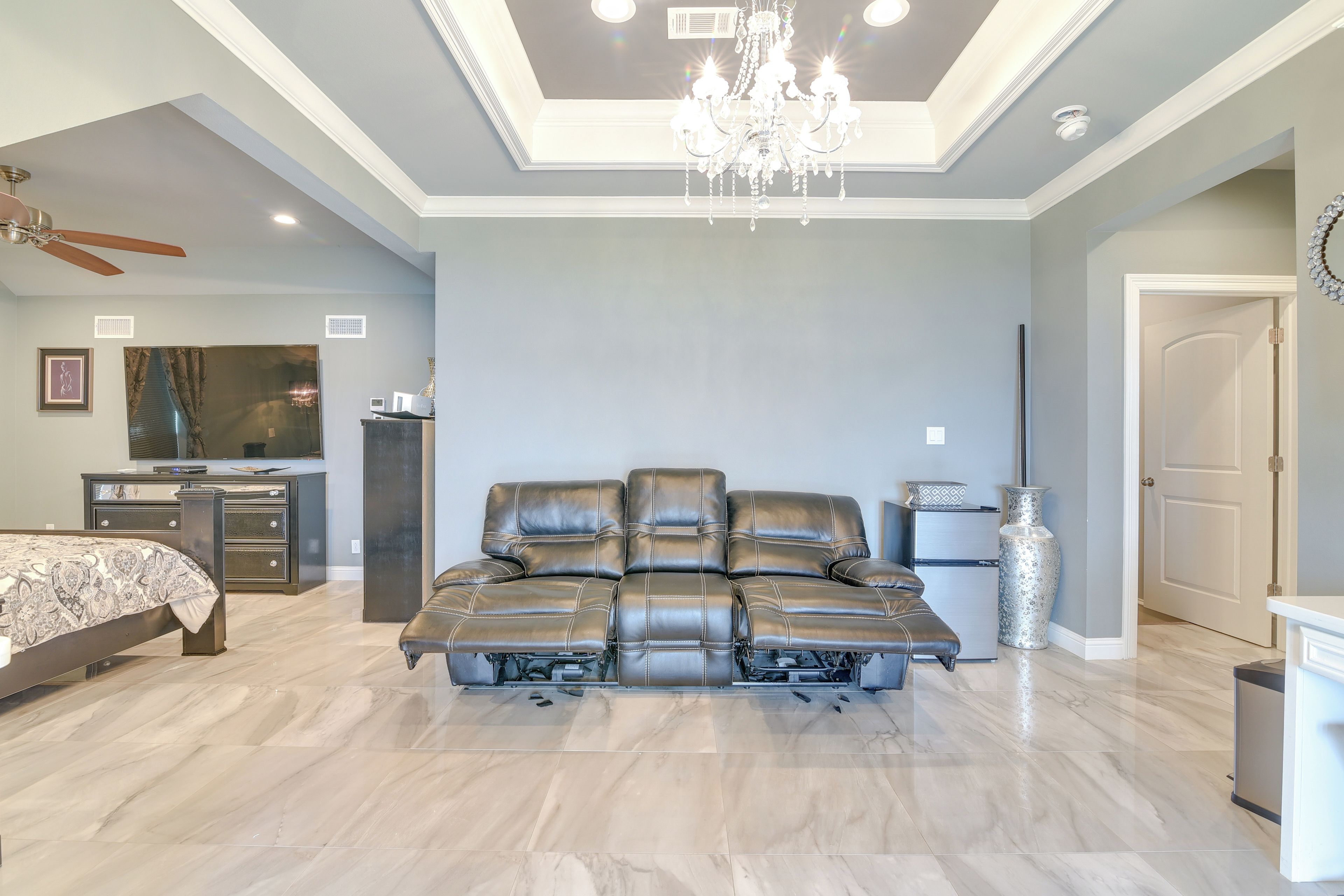 A spacious bedroom with a large sectional sofa, a bed, a desk, and a chandelier.