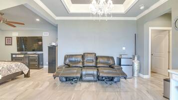 A spacious bedroom with a large sectional sofa, a bed, a desk, and a chandelier.