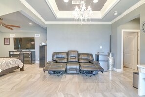 A spacious bedroom with a large sectional sofa, a bed, a desk, and a chandelier.