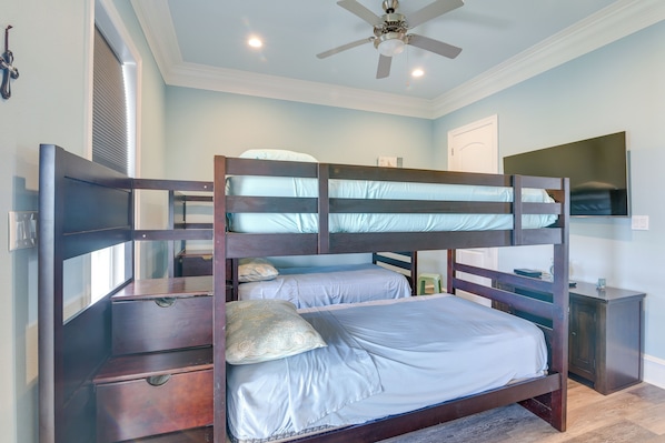A bunk bed with two levels, a ceiling fan, a bedside table, and a TV on the wall.