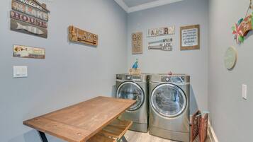 A laundry room with two front-loading washing machines, a wooden table, and various decorative signs on the walls.