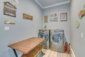 A laundry room with two front-loading washing machines, a wooden table, and various decorative signs on the walls.