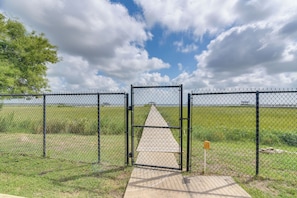 A fenced area with a gate, a concrete path, and a grassy field.