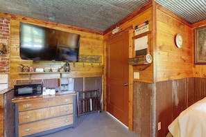 A rustic cabin interior with a television, kitchenette, wooden walls, and a door with a warning sign. - Countryside Escape! Cozy Studio w/ Patio (Chillicothe)