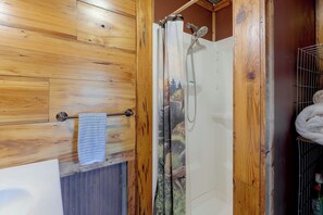 A wooden bathroom with a shower, a towel rack, and a metal rack with towels.