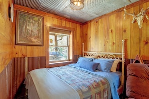 A wooden room with a bed, a painting, and a window.