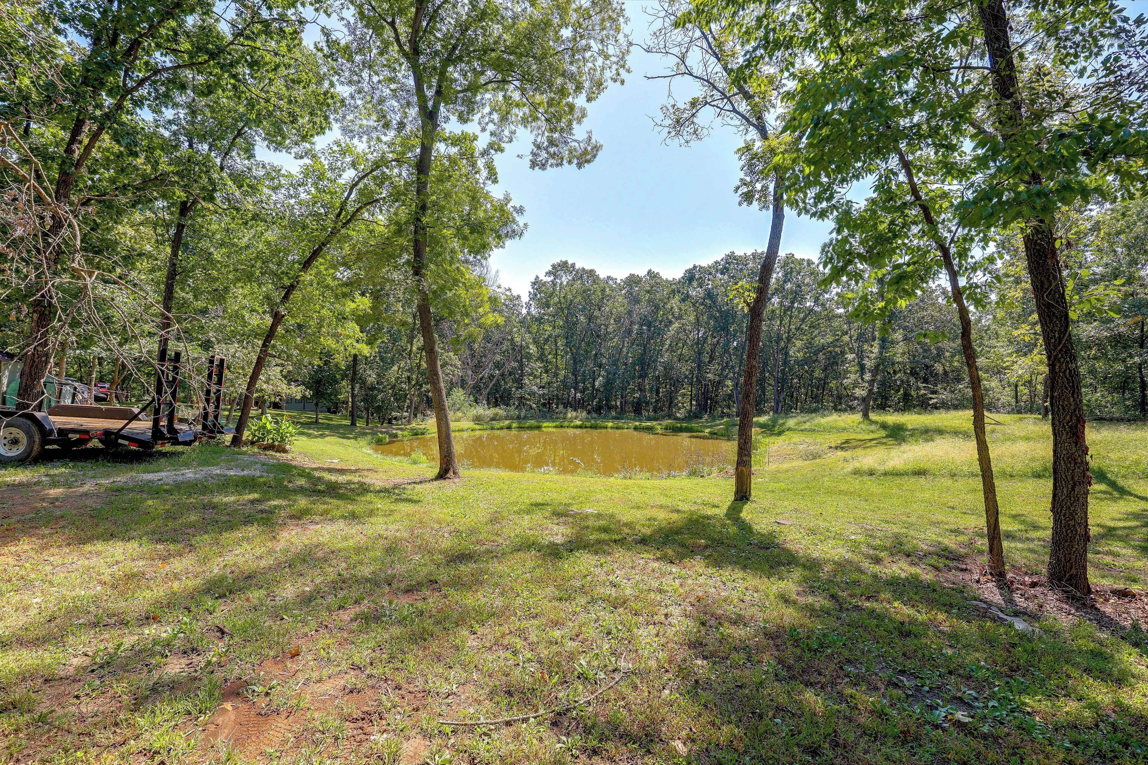 A natural landscape with a pond, trees, and a trailer.