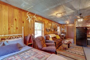 A cozy cabin interior with a bed, two sofas, a dining area, and a refrigerator.