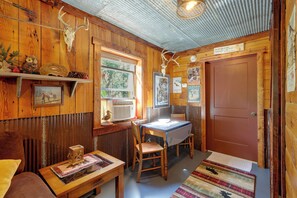 A rustic interior with wooden walls, a dining table, chairs, a bench, and a fireplace.