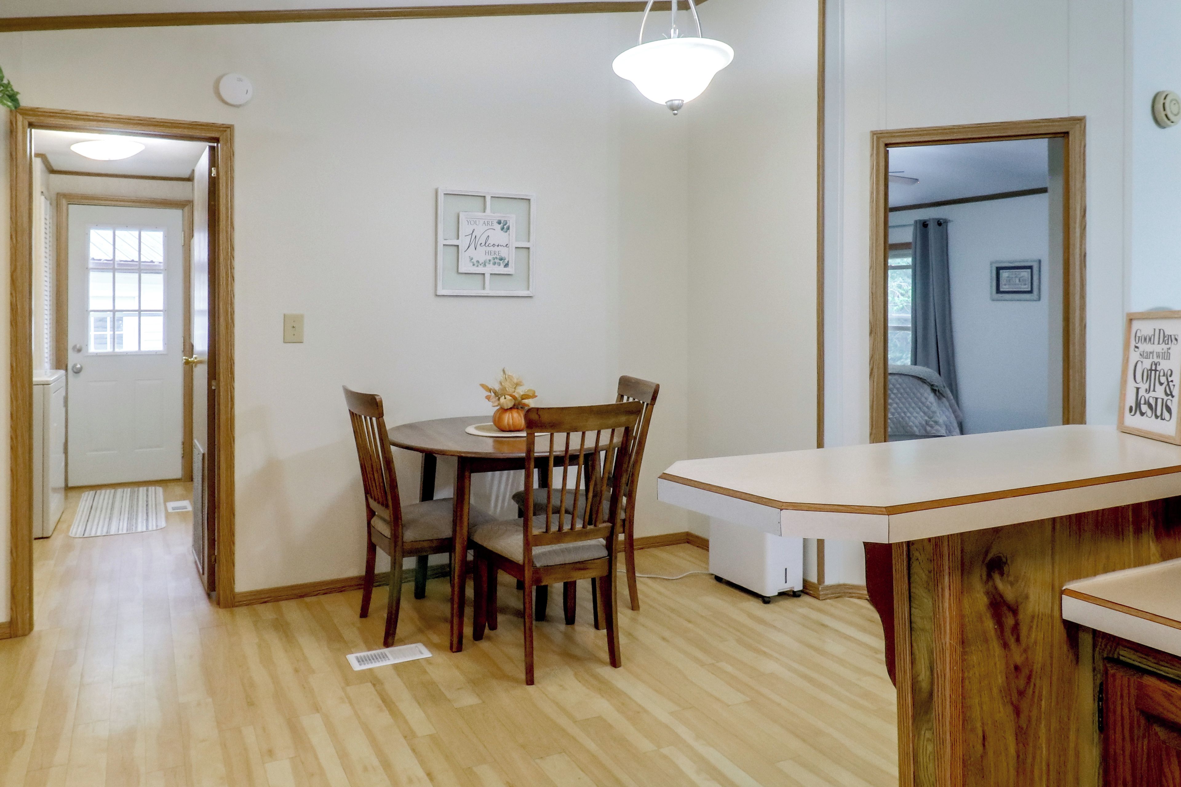 A dining area with a wooden table and chairs, a white ceiling light, and a welcome sign on the wall.