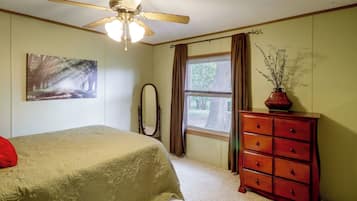 A bedroom with a bed, a dresser, a window with curtains, a ceiling fan, and a painting on the wall.