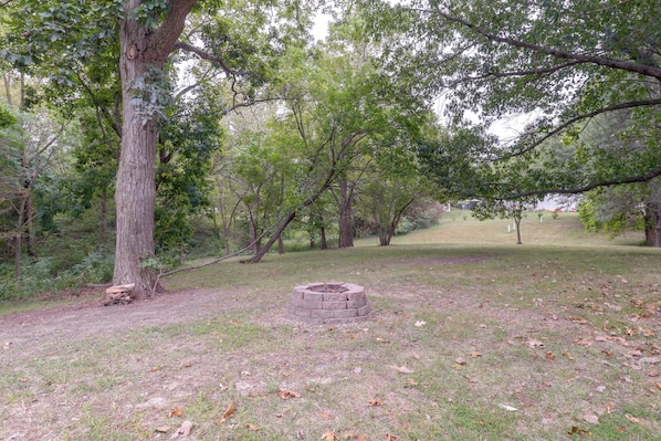 A natural outdoor area with a circular stone fire pit surrounded by grass and trees.