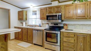 A kitchen with wooden cabinets, stainless steel appliances, a microwave, oven, dishwasher, and a window with curtains.