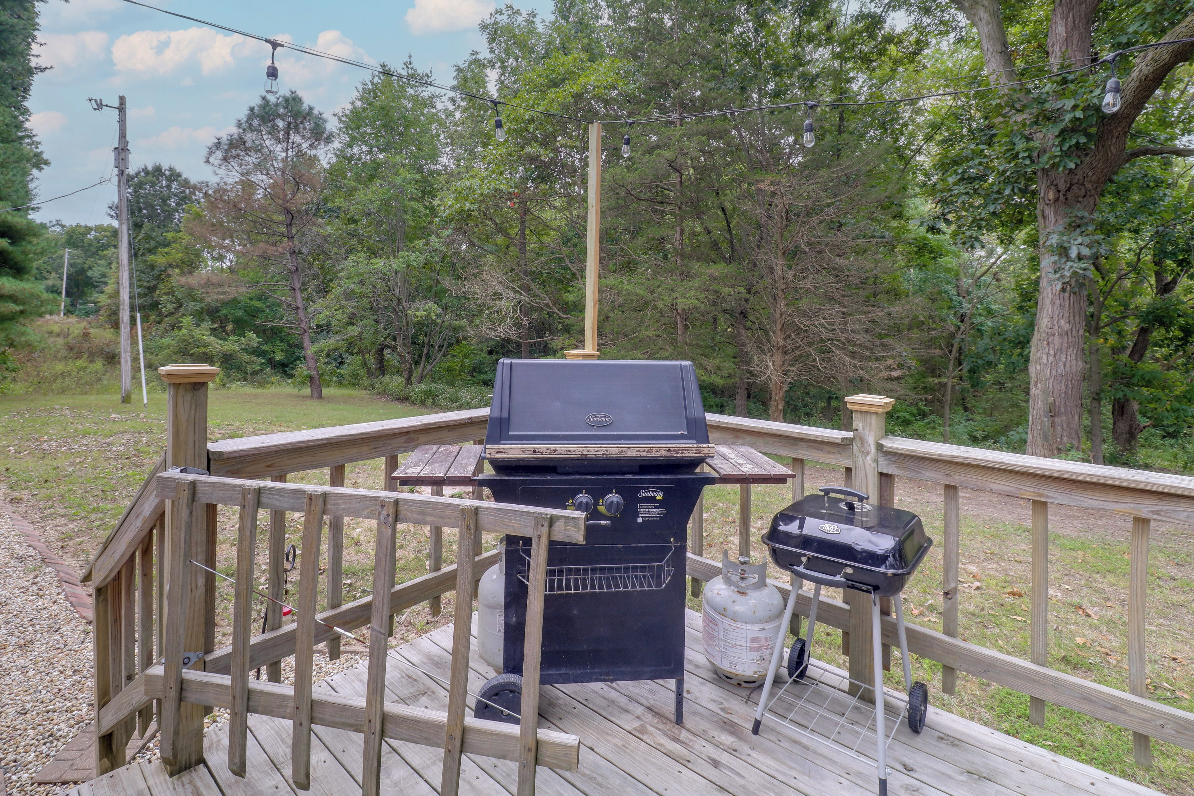 A deck with a barbecue grill and a gas tank, surrounded by a wooden railing and trees.