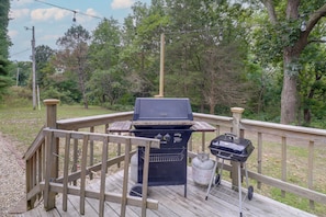 A deck with a barbecue grill and a gas tank, surrounded by a wooden railing and trees.