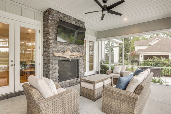A covered patio with wicker furniture, a stone fireplace, and a ceiling fan.