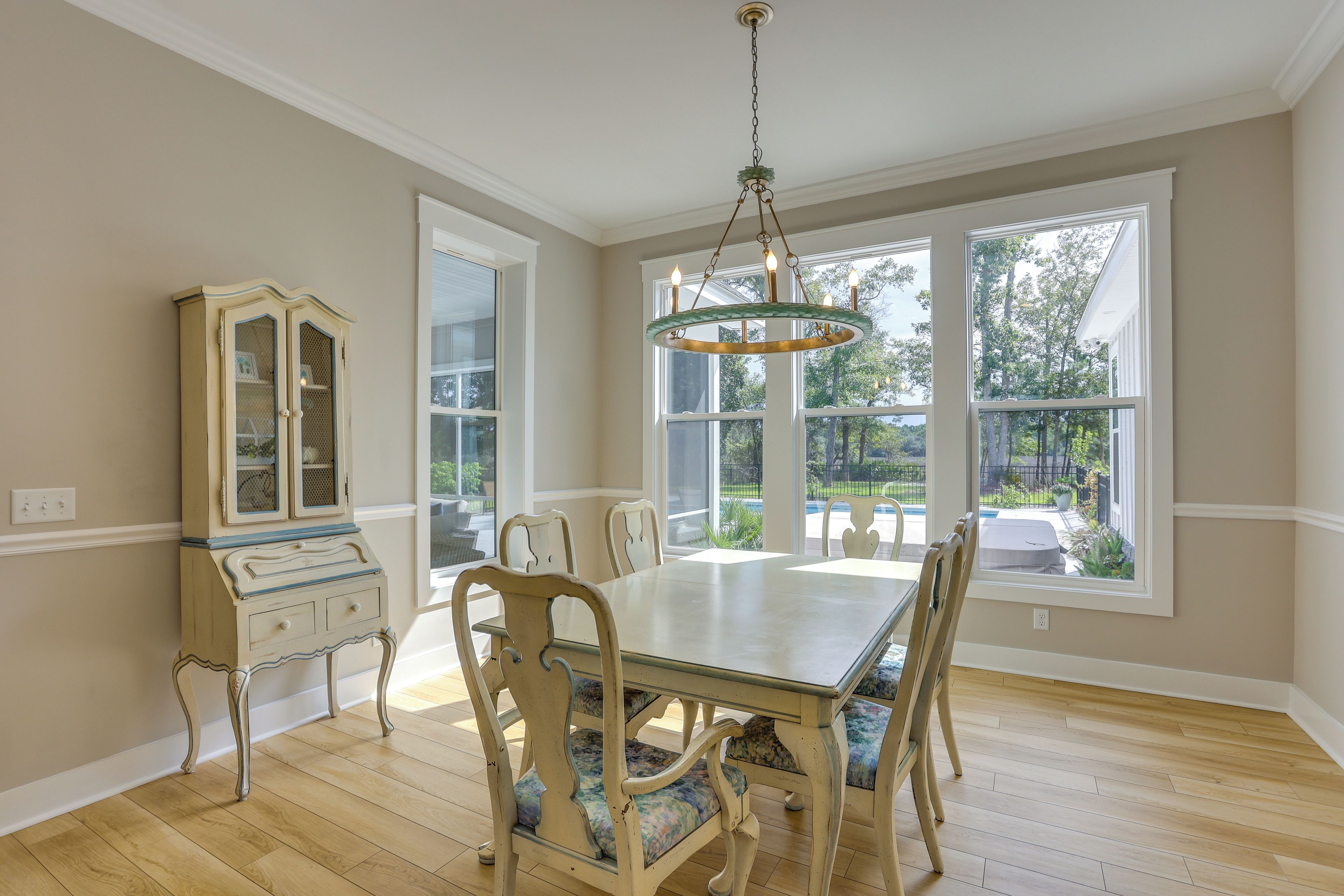A dining room with a large table, chairs, a chandelier, and a cabinet.