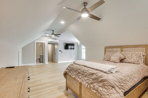 A bedroom with a sloped ceiling, a ceiling fan, a bed with a wooden headboard, and a wooden floor.