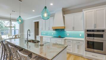A modern kitchen with white cabinetry, a central island with stools, a stainless steel oven, and teal backsplash.