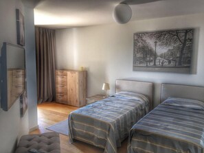 Ein Schlafzimmer mit zwei Betten, einem Holzschrank, einer Lampe und einem Stadtbild im Bilderrahmen.
