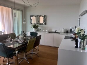 A modern kitchen with a dining area, white cabinets, a large mirror, and a dining table set for four. - Holiday Home 'Aurora Elegant Lake View' with Lake View, Shared Pool and Wi-Fi (Toscolano Maderno)