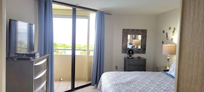 Habitació d'hotel amb llit, televisió, calaixera, mirall i balcó amb cortines.