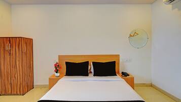 A hotel room with a bed, bedside table, a clock on the wall, and an air conditioning unit.