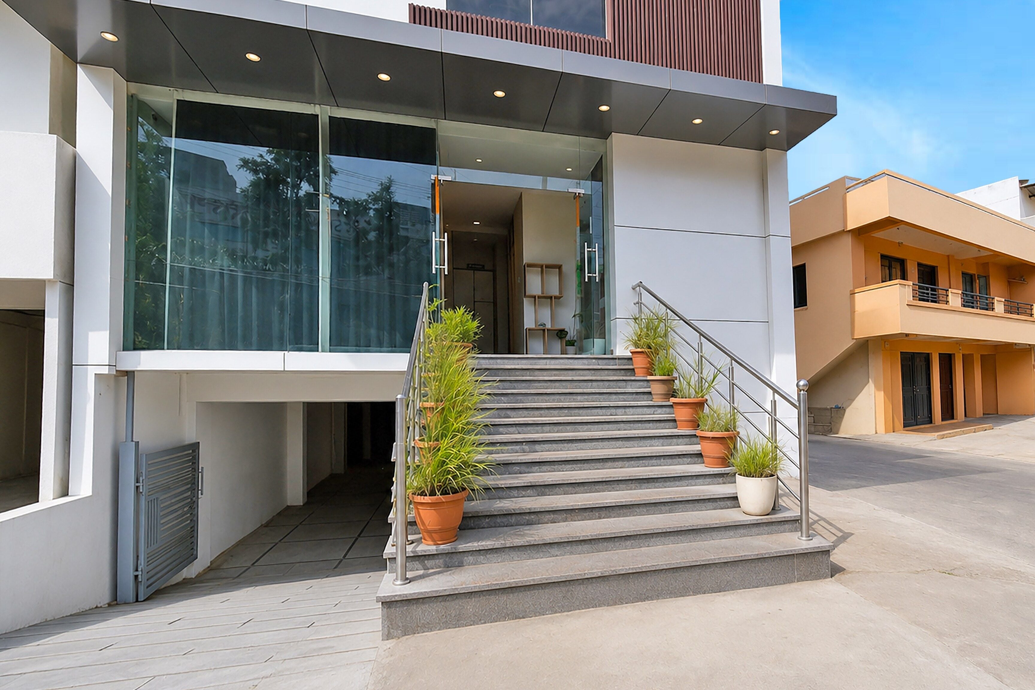 A modern building with a glass entrance, a staircase with potted plants, and a metal railing.