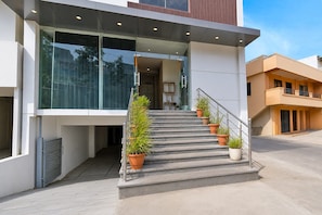Un edificio moderno con entrada de vidrio, una escalera con plantas en macetas y una barandilla de metal.