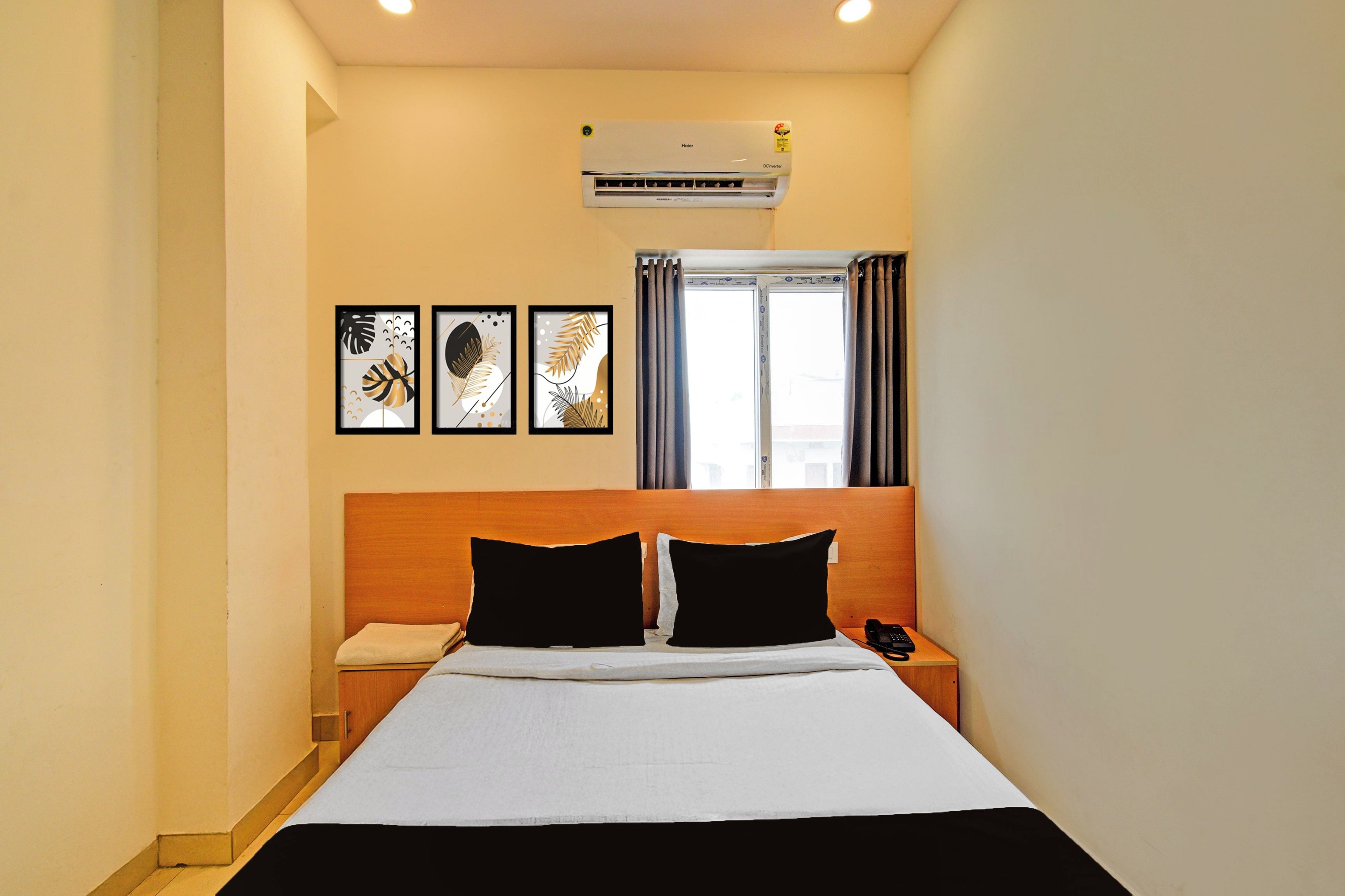 Una habitación de hotel con cama, mesita de noche, teléfono y unidad de aire acondicionado.