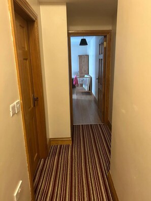 A hallway with a striped carpet, wooden doors, and a view into a room with a bed and a wardrobe. - Greencastle – 4-Bed Townhouse Sleeps 8 | Free Parking | Mourne Mountains (Kilkeel)