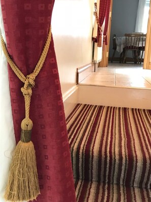 Ein Zimmer mit Streifenmuster-Teppich, einem roten Vorhang mit einer Kordelverzierung und einem Holzstuhl im Hintergrund.